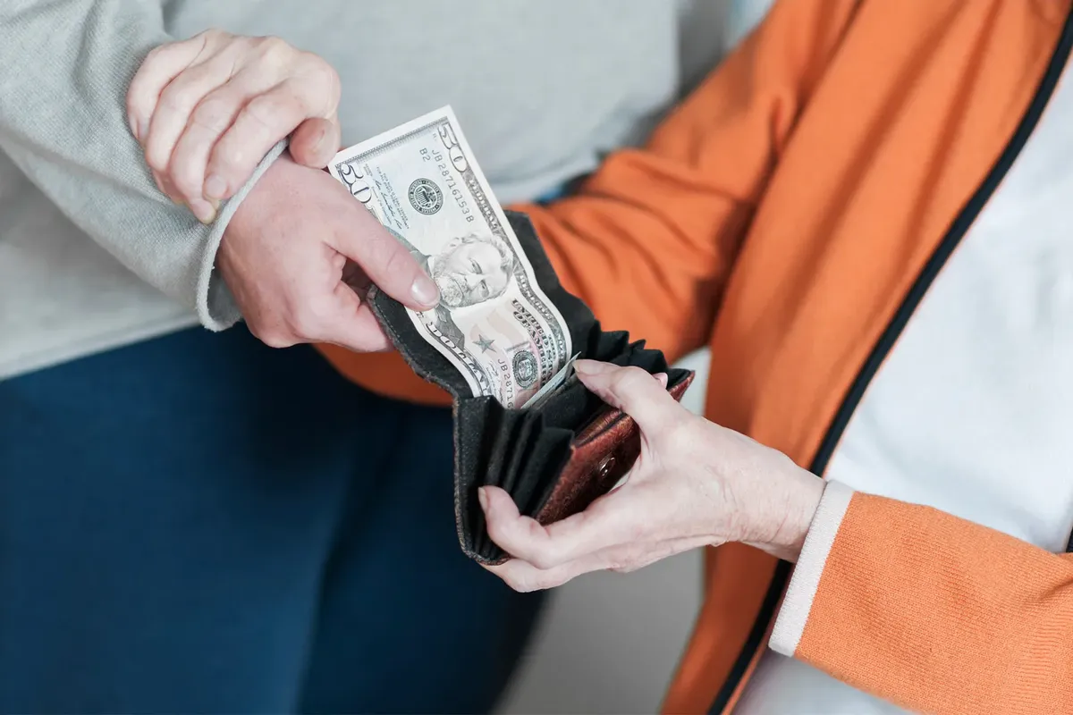 Elderly woman handing money to younger woman, illustrating intergenerational financial support.