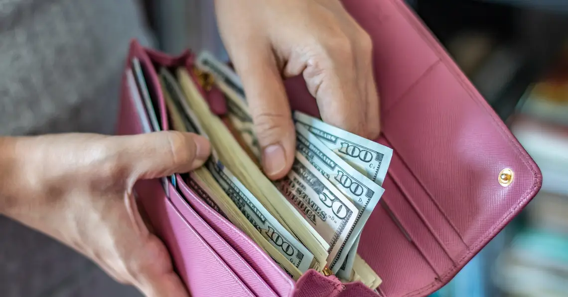 Middle-aged woman looking at her wallet, pulling out a single dollar bill, highlighting financial stress and budgeting concerns.